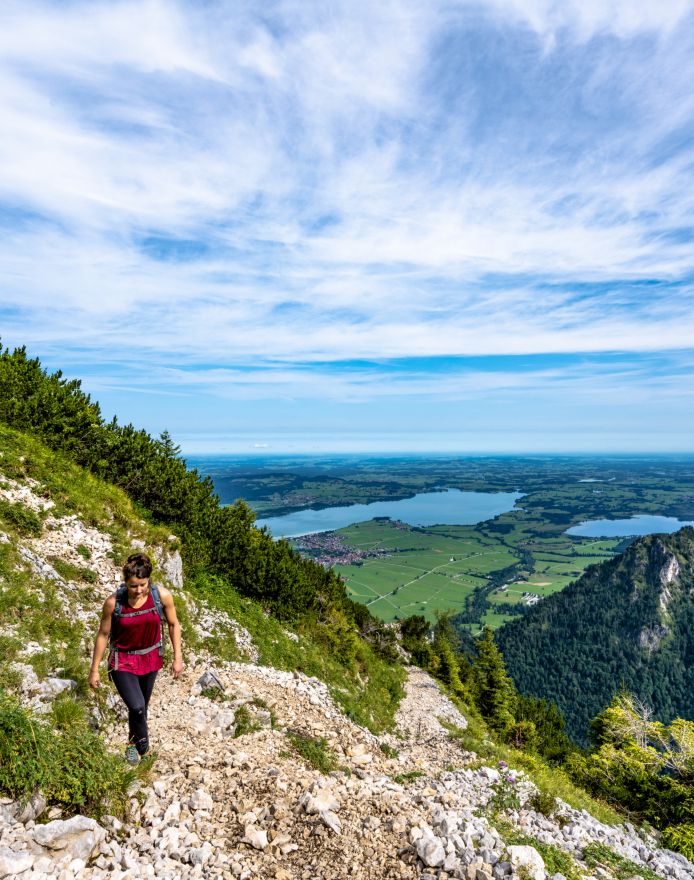 Frau geht wandern auf einem Berg, im Hintergrund sind Seen zu erkennen.